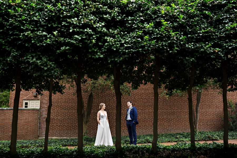 A bride and groom stand between trees in a Philadelphia park.